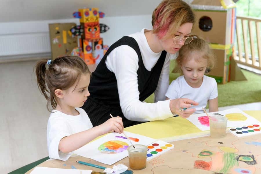 A nursery practitioner painting with two children at a table