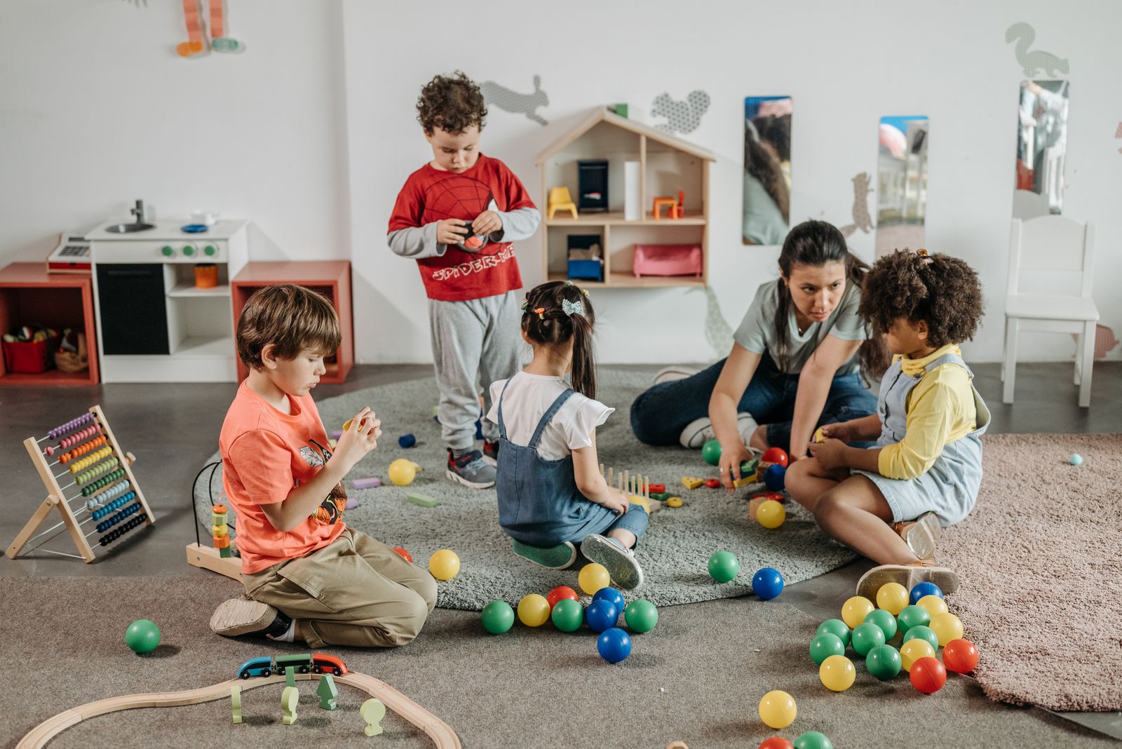 Children and an educator playing with wooden toys on a rug in a bright nursery room